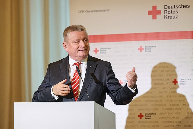 DRK-Präsident Hermann Gröhe spricht vor einem Mikrofon. Im Hintergrund das Logo des Deutschen Roten Kreuzes