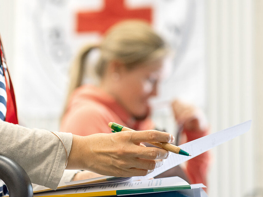 Foto: Zwei Frauen über Unterlagen gebeugt - im Hintergrund das DRK-Logo