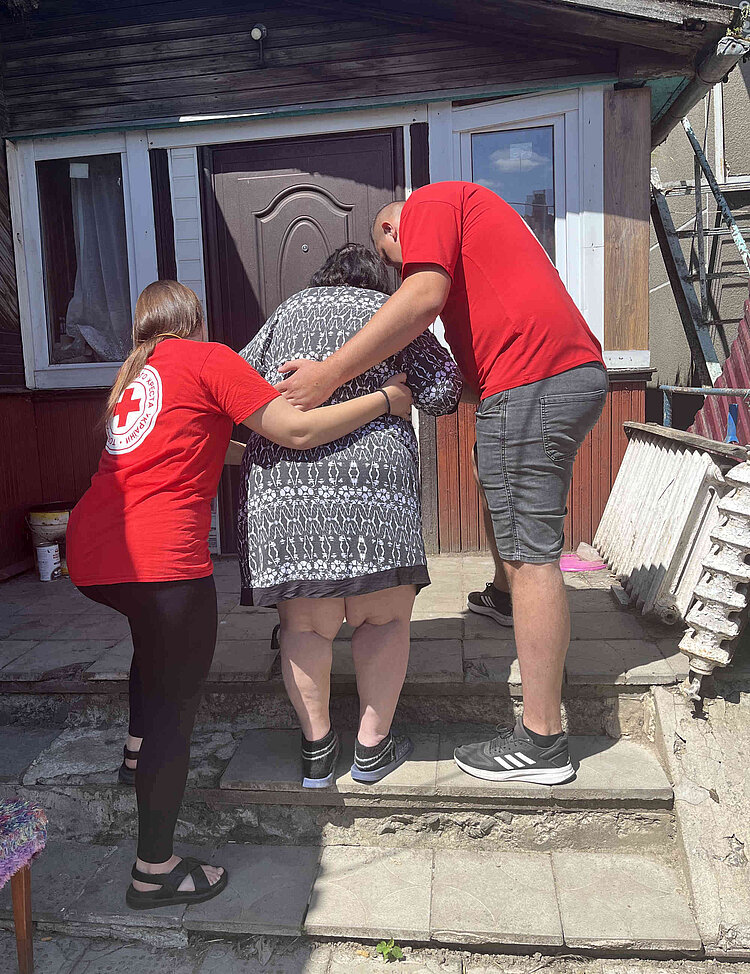 Gesundheitsprojekt des Ukrainischen Roten Kreuzes Zwei Mitarbeitende des URK mit Rotkreuzkleidung helfen einer älteren Person beim Treppensteigen