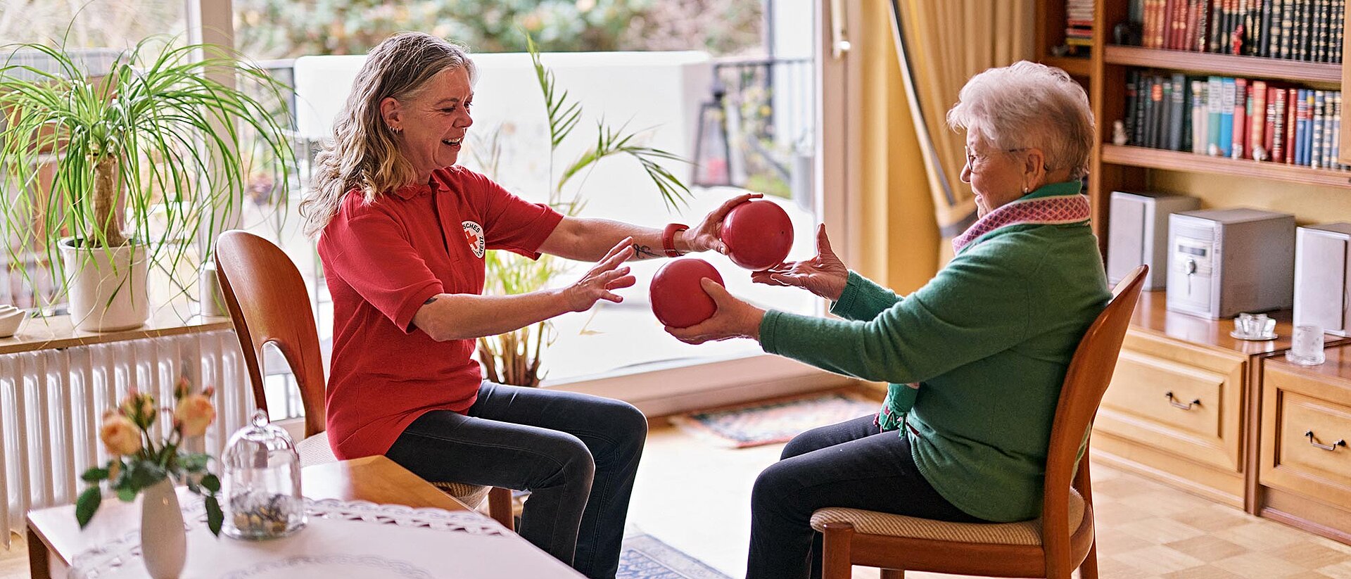Seniorin und DRKlerin bei Sitzgymnastik mit Bällen