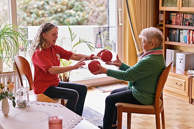 Seniorin und DRKlerin bei Sitzgymnastik mit Bällen