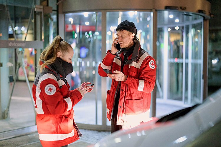 DRKlerin und DRKler vor Drehtür an Smartphones
