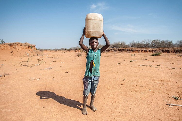 Junge mit Wasserkanister vor Wüste