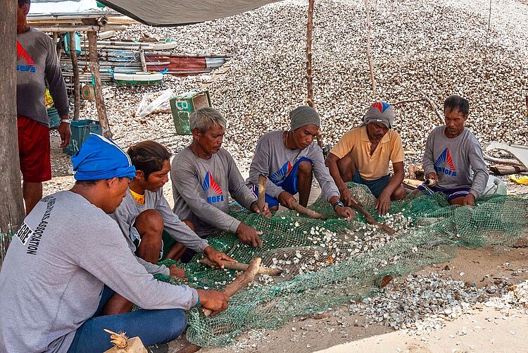 Männer mit Fischernetzen und Muscheln auf Boden