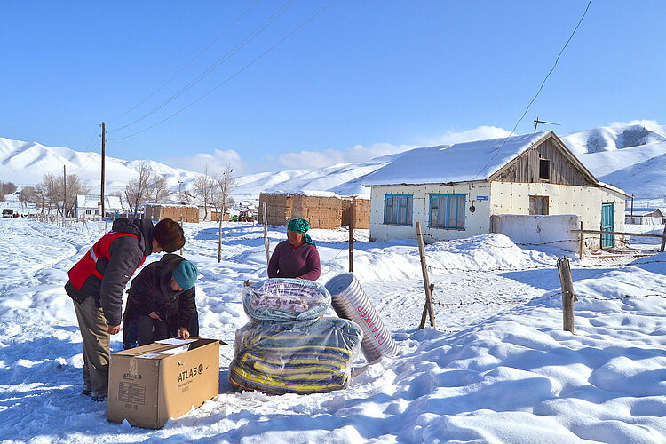 Vorrausschauende humanitäre Hilfe in Kirgistan Drei Menschen mit Hilfsgütern im Schnee
