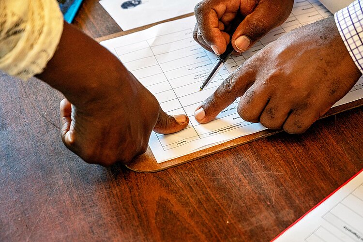 Eswatini: Humanitäre Geldleistungen Mann presst Finger auf Papier