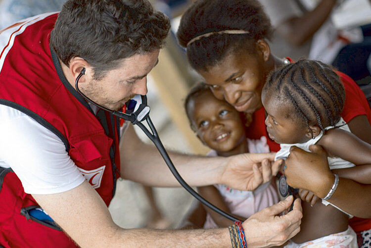Gesundheitsversorgung Foto: Arzt untersucht ein Mädchen auf dem Schoß ihrer Mutter in Haiti