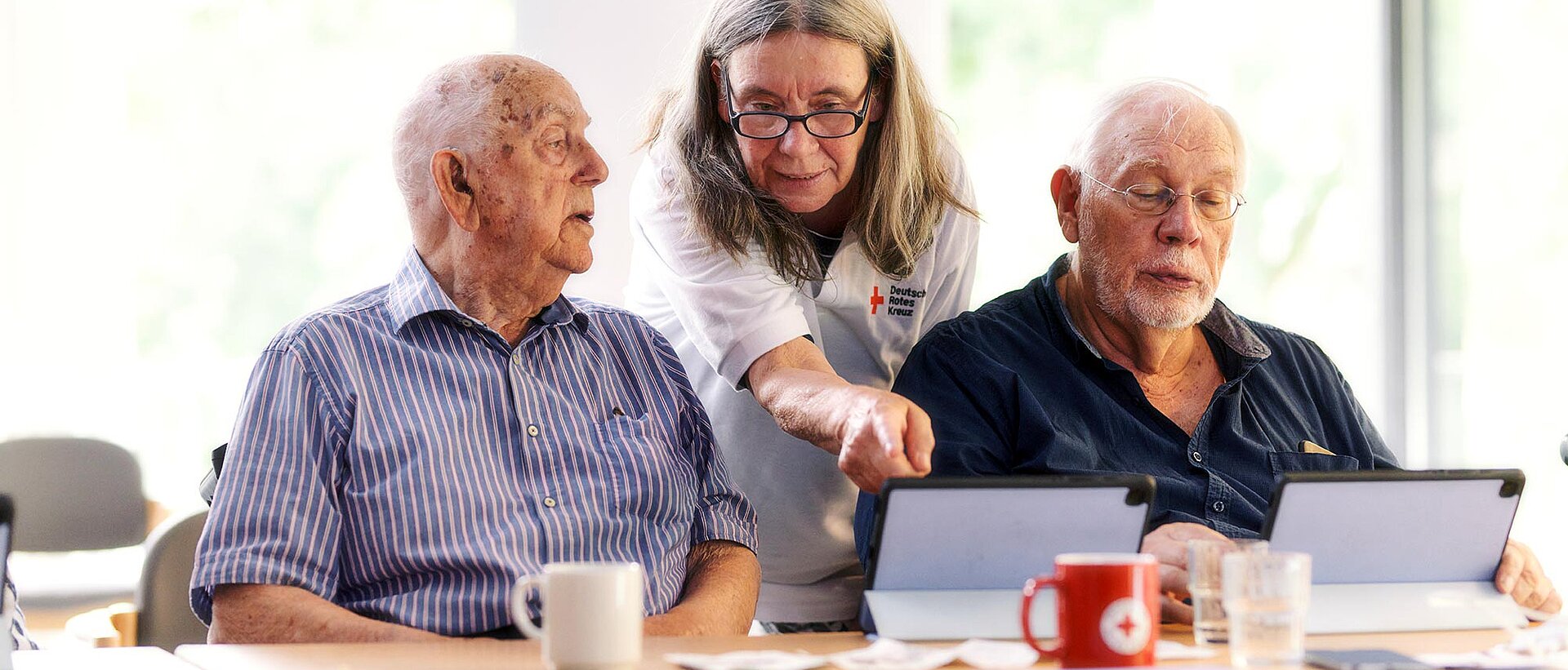 DRKlerin und Senioren schauen auf Tablets