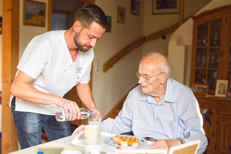 Pfleger schenkt Senior Wasser ein