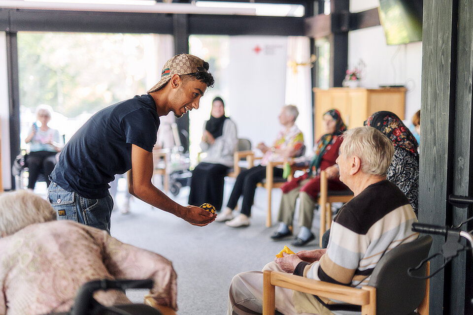 Pflegeheim-Aktivitäten Junger Mann reicht Senior einen Ball