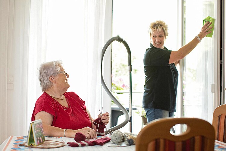 Pflegerin putzt Fenster bei Seniorin