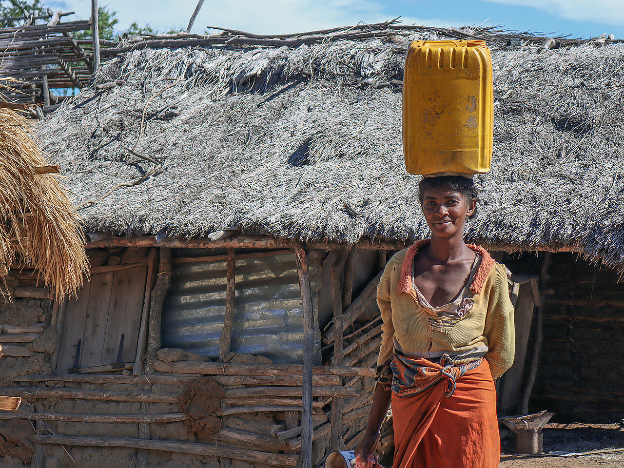 Madagassin mit Wasserkanister auf Kopf vor Hütte