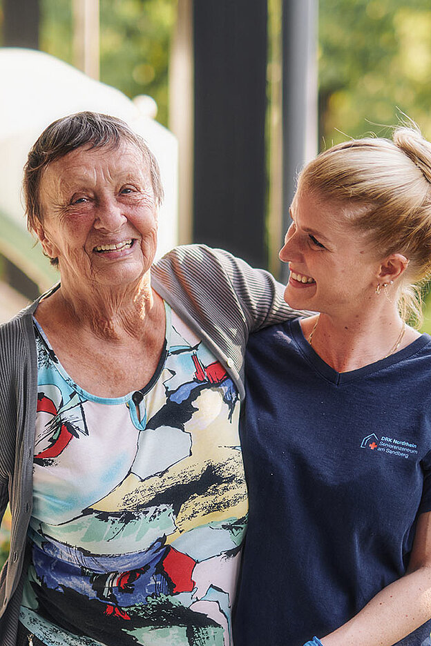 Seniorin lacht mit DRKlerin auf Balkon