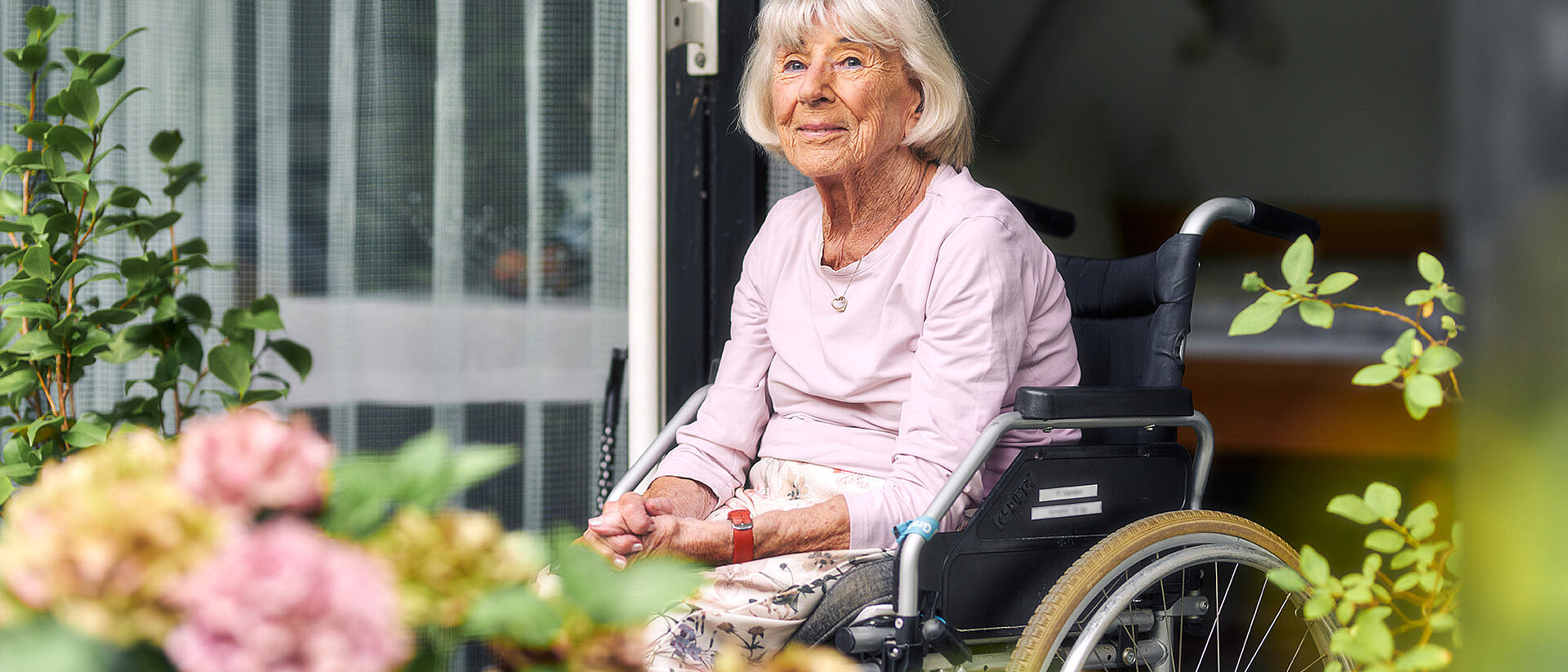 DRK-Leistungen in Deutschland Seniorin im Rollstuhl auf Balkon mit Blumen