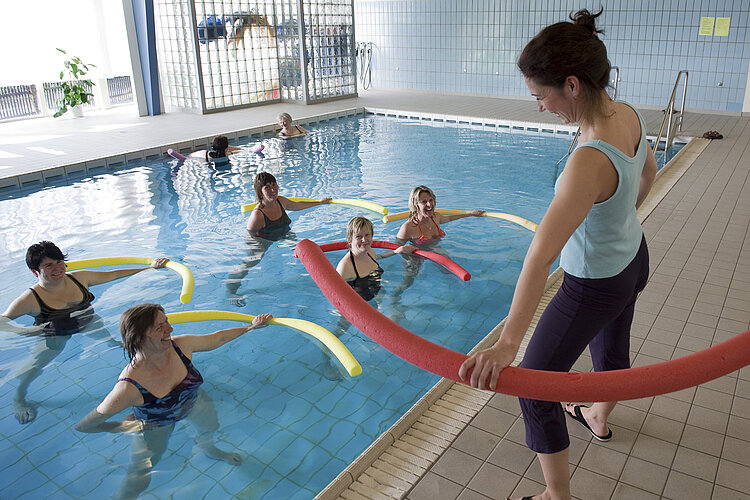 Wassergymnastik Frauen mit Schwimmnudeln im Schwimmbecken