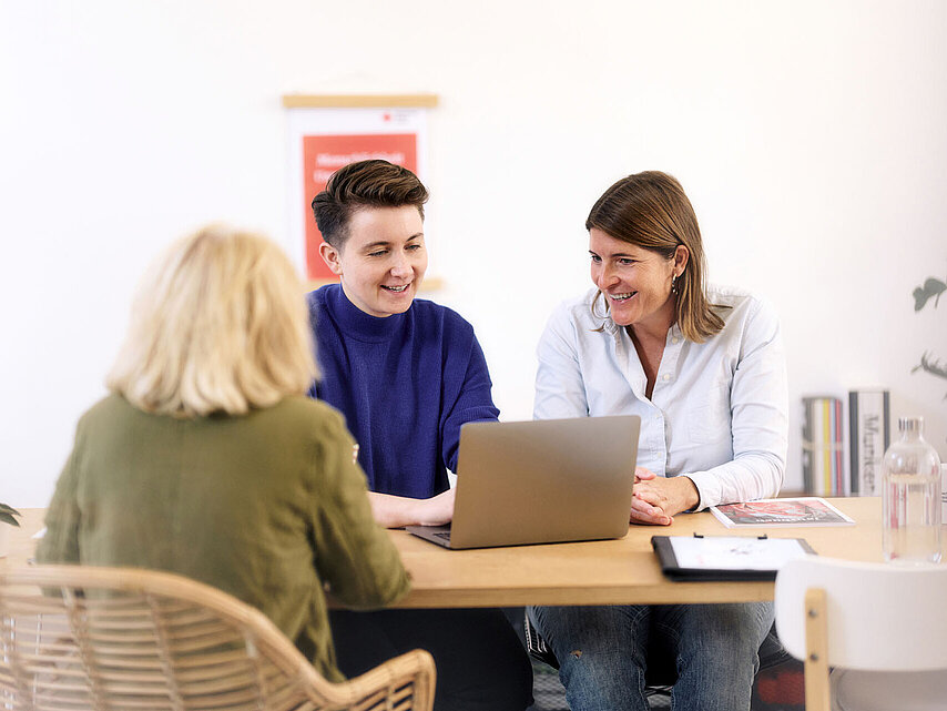 Drei Frauen lächelnd im Gespräch am Laptop