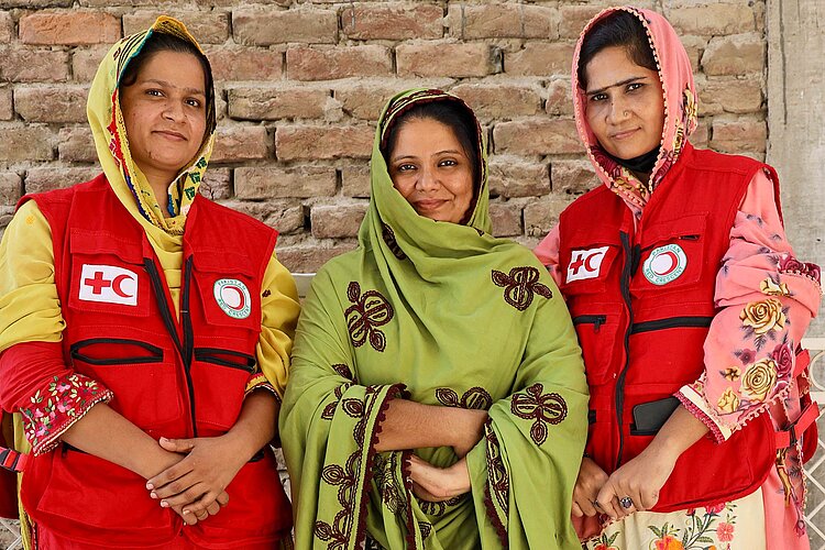 Drei pakistanische Frauen - zwei in Rothalbmond-Kleidung