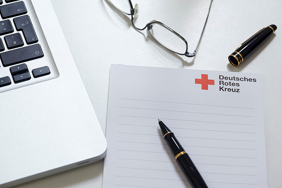 Laptop, Brille, Stift und Rotkreuz-Block