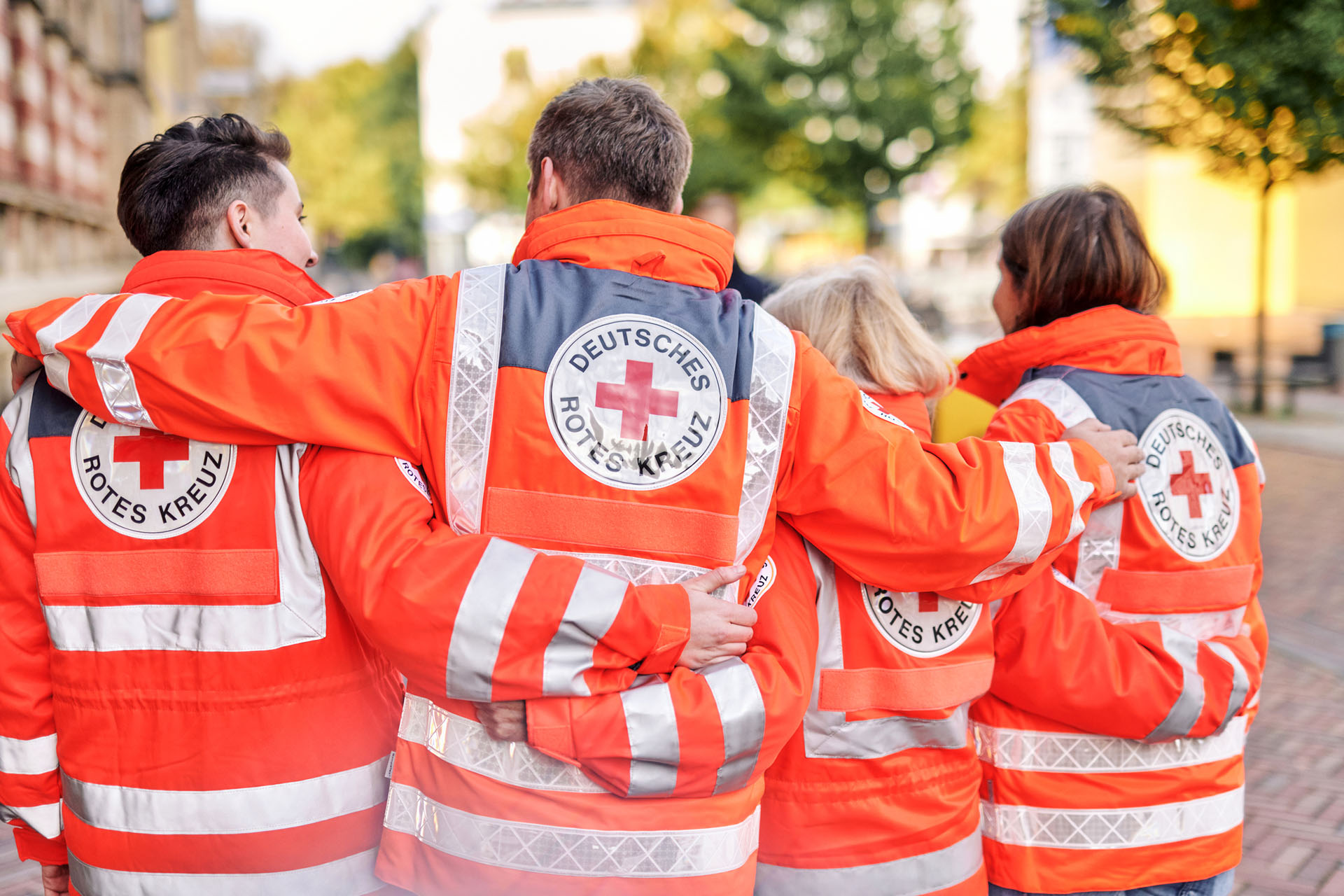 Teamarbeit im Einsatz Vier DRKler in Einsatzjacken legen Arme über Schultern
